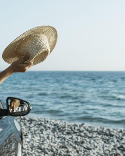 mid-shot-woman-hand-out-car-window-holding-hat-near-sea_23-2148756489